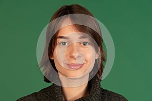 Cropped portrait of young woman looking at camera, barely smiling, posing isolated ove green background