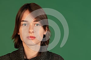 Cropped portrait of young woman looking at camera, posing isolated ove green background. Serious look