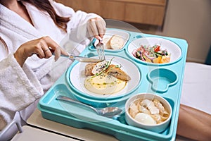 Cropped pregnant woman cutting meat with knife and fork during having lunch