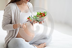 Cropped of pregnant woman eating healthy vegetable salad, bedroom interior