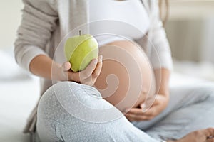 Cropped of pregnant woman holding apple and touching belly