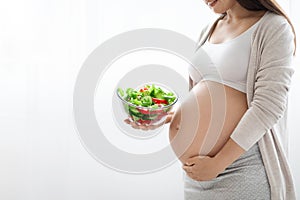Cropped of pregnant woman showing healthy vegetable salad, side view