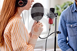 Cropped Redhead woman singing to the microphone in studio. Female vocal. Side View
