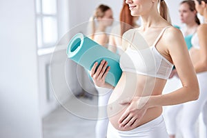 cropped relaxed pregnant woman stand holding fitness mat in hands photo