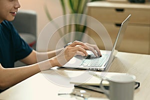 Cropped shot of asian man sitting in cozy living room and surfing internet with laptop computer