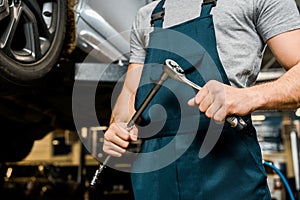 cropped shot of auto mechanic with lug wrench in hands