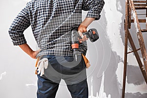 Cropped shot of back of a man holding drill on his hips while looking at wall