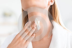 Cropped shot of blonde lady applying moisturizer on neck skin