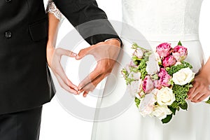 cropped shot of bride with bouquet and groom making heart sign with hands