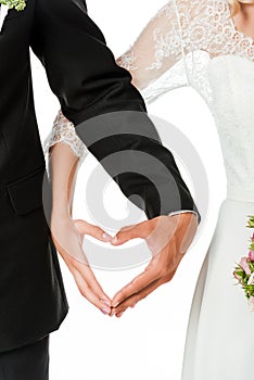 cropped shot of bride and groom making heart sign with hands