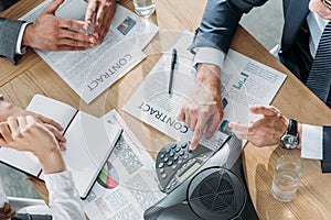 cropped shot of business people having conversation with contracts and speakerphone on table photo