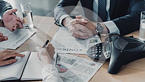 cropped shot of business people having conversation with documents and speakerphone on table