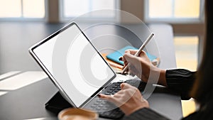 Cropped shot of business woman typing on keyboard of tablet and holding electric pen in hand.