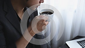 Businessman drinking coffee and reading news on laptop computer.
