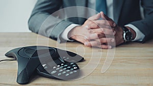 cropped shot of businessman sitting behind conference phone on table