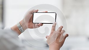 Cropped shot of  businessman touching horizontal blank screen smartphone with blurred office room