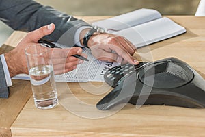 cropped shot of businessman using conference phone on table