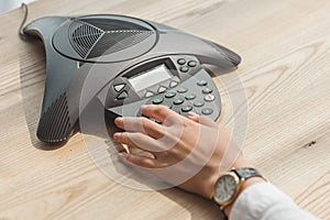 cropped shot of businesswoman pushing button of speakerphone on wooden table