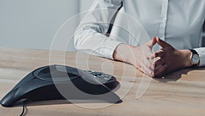 cropped shot of businesswoman in white shirt sitting in front of conference phone and waiting