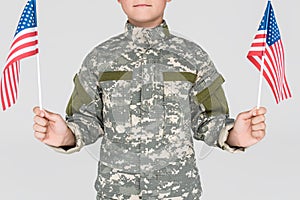 cropped shot of child in military uniform with american flagpoles in hands
