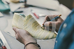 cropped shot of cobbler holding pencil and working with unfinished footwear