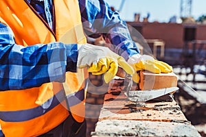 Cropped shot of construction worker in protective gloves laying bricks