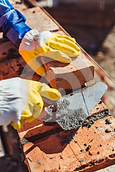 Cropped shot of construction worker in protective gloves laying bricks