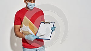 Cropped shot of delivery man wearing face mask and protective gloves holding parcels and envelopes, showing form for