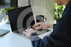 Cropped shot of IT developer typing on laptop with programming code on computer screen
