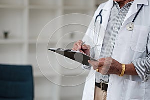 Cropped shot of doctor in uniform with stethoscope taking note patient medical history on clipboard