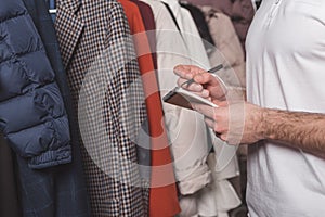 cropped shot of dry cleaning worker with notepad counting clothes on hangers