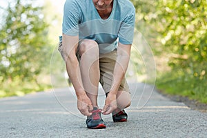 Cropped shot of elderly male athlete ties shoelaces, takes rest after jogging exercise, wears sportswear, poses outdoor. Man runne