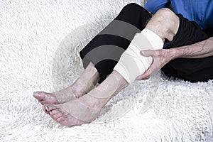 Cropped shot of elderly man sitting on sofa and suffering from leg pain. Leg with bandage.