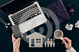 Cropped shot of family lawyer using smartphone at workplace with house and family cut out figures