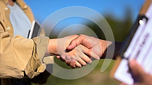 Cropped shot of farmers shaking hands at the field against blue sky. Agreement and contract in agriculture