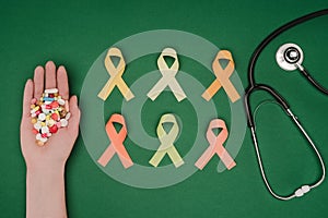 cropped shot of female hand with pills, arranged colorful ribbons and stethoscope