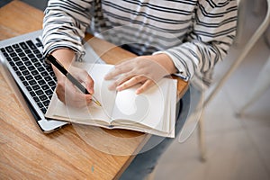 A cropped shot of a female student doing homework or taking notes in her notebook at a table