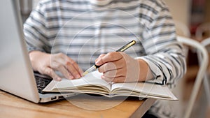A cropped shot of a female student doing homework or taking notes in her notebook at a table