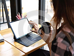 Cropped shot of female teenager holding cup and using digital tablet on wooden table in cafe