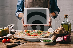 Cropped shot of food blogger in apron holding tablet with blank screen at tabletop