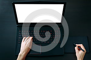 Cropped shot of graphic designer`s hands working on graphic tablet and laptop with blank screen on black office table. Freelance,