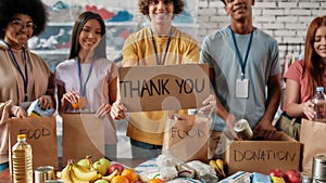 Cropped shot of group of diverse young volunteers packing food and drinks donation, Guy holding card with Thank you