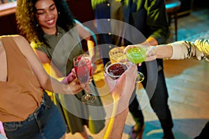 Cropped shot of group of friends, young adults, men and women having fun, toasting, drinking cocktails standing in a