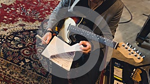 cropped shot of a guitarist holding sheets of notes and sitting on the floor