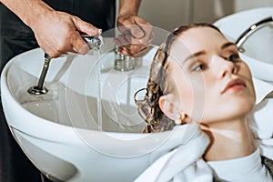 Cropped shot of hairdresser checking water and washing hair to young woman