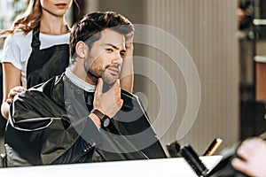 Cropped shot of hairdresser doing hairstyle to handsome man looking at mirror