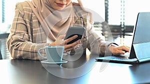 Cropped shot of happy muslim woman using smart phone while sitting in her office.