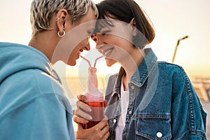 Cropped shot of happy young lesbian couple drinking from one glass bottle with the straw, Two women enjoying cold