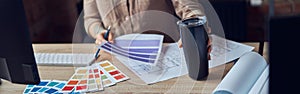 Cropped shot of interior designer working on project, looking at color swatches, holding bottle while sitting at