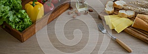Cropped shot of kitchen table with French baguette, cheese, vegetables on wooden kitchenware